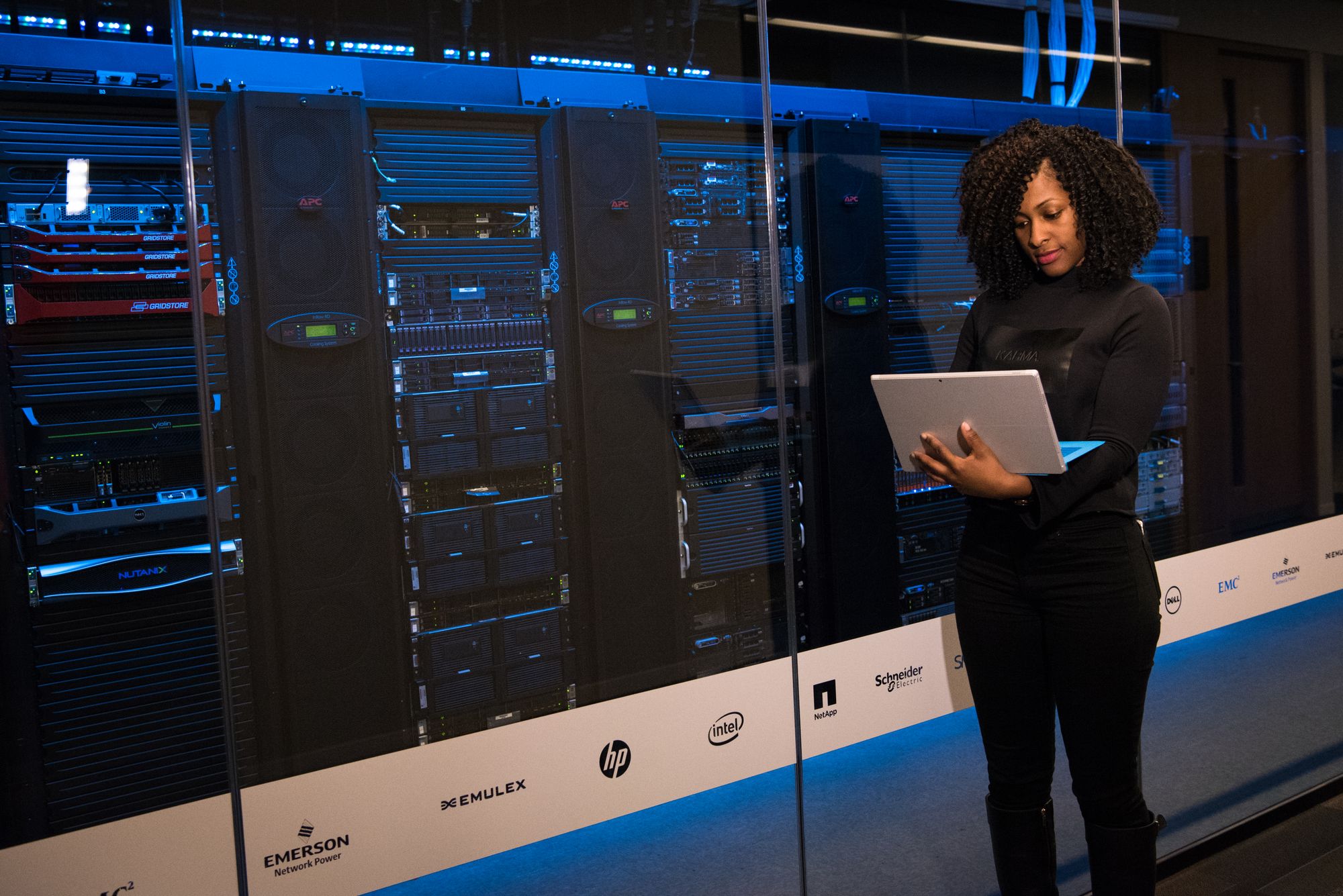 Engineer using a tablet while monitoring blue-lit server infrastructure.
